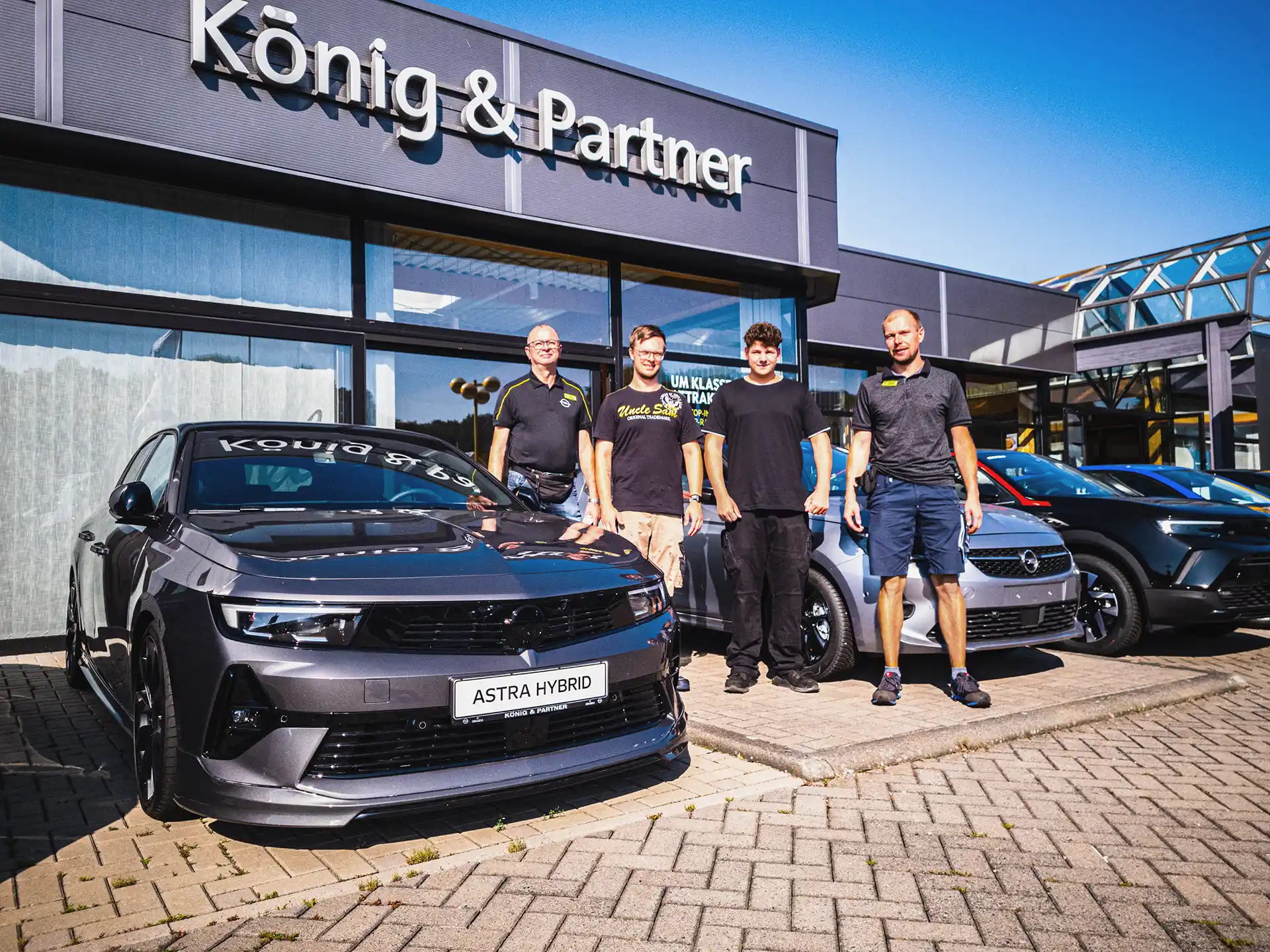 2 Kfz-Mechatroniker-Azubis mit Serviceleiter und Werkstattmeister vor dem Autohaus König & Partner