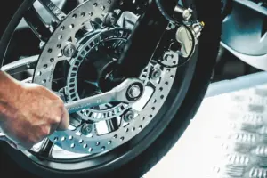 Symbolbild Hand schraubt mit Werkzeug an Motorradreifen - Stellenangebot Zweiradmechatroniker/-in (m/w/d)