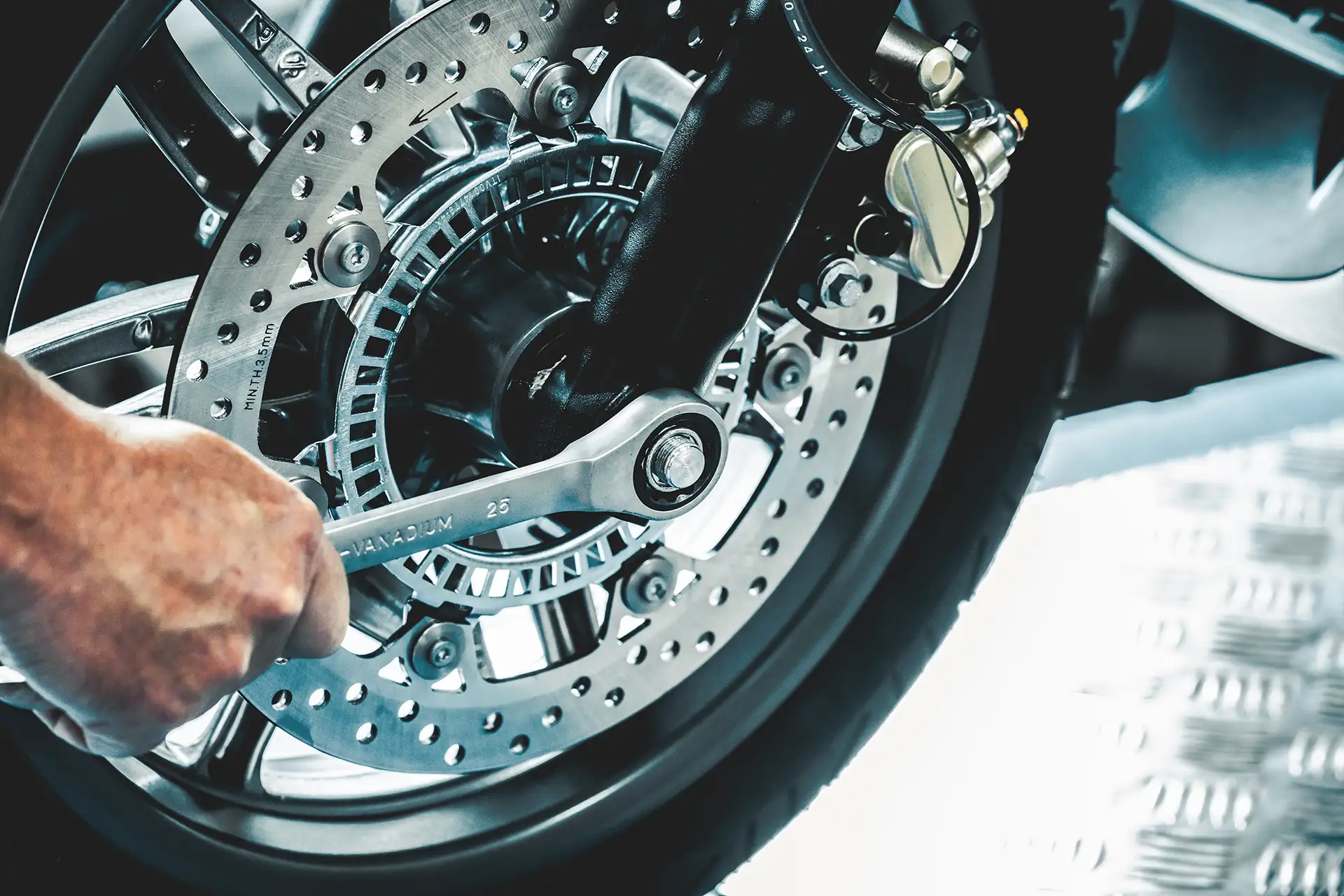 Symbolbild Hand schraubt mit Werkzeug an Motorradreifen - Stellenangebot Zweiradmechatroniker/-in (m/w/d)