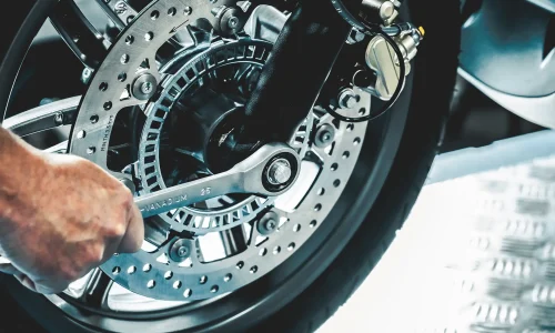 Symbolbild Hand schraubt mit Werkzeug an Motorradreifen - Stellenangebot Zweiradmechatroniker/-in (m/w/d)
